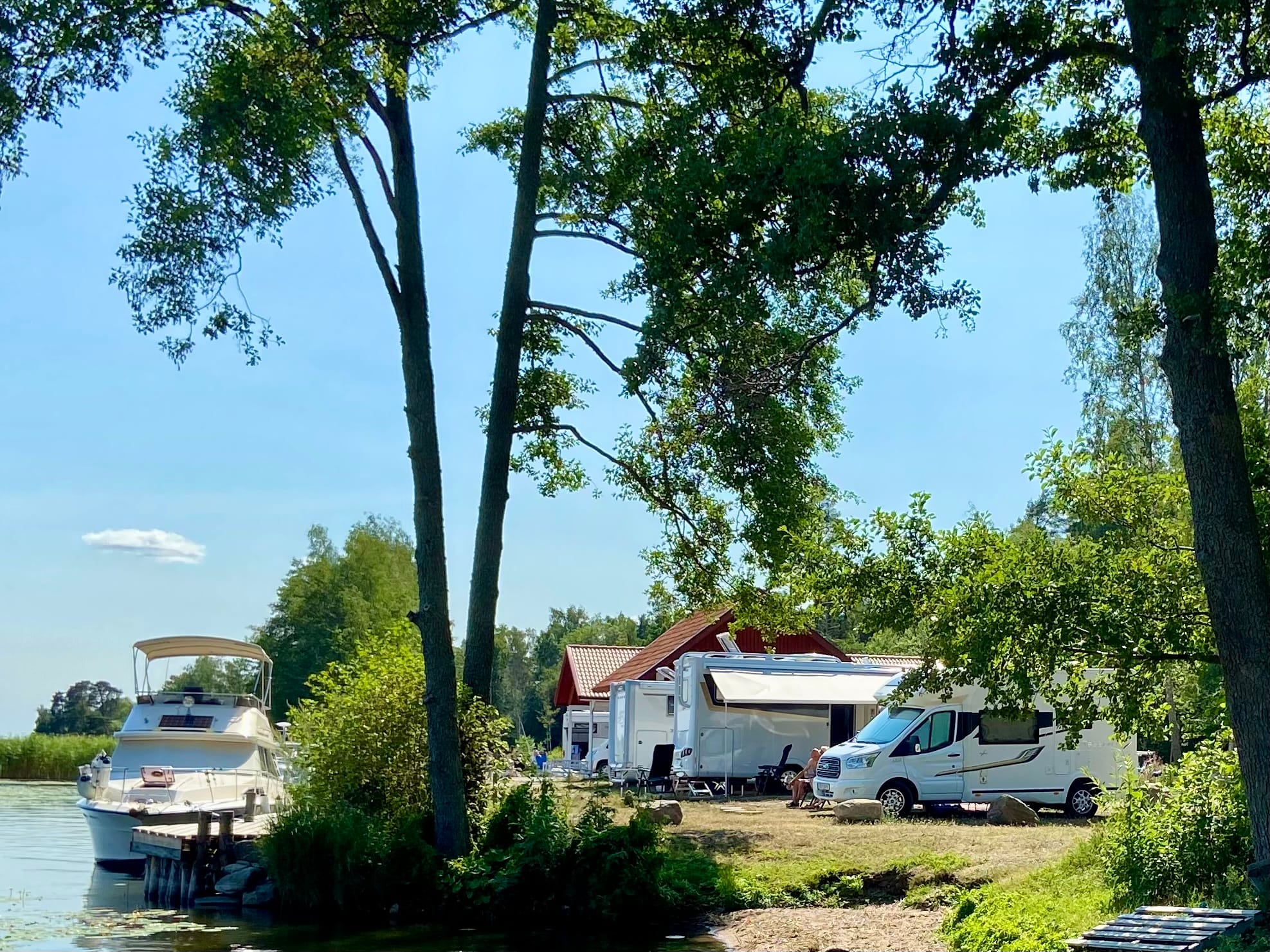 Ställplats Lungershamn Snötäckt väg kantad av träd, byggnad och rött staket.